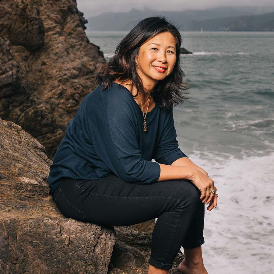 Perfumer and Nose Yosh Han sitting on the rocky shoreline of San Fransisco 